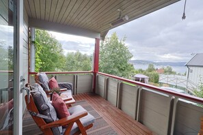 A covered outdoor seating area with wooden chairs and cushions, overlooking a body of water and greenery. - Aurora House – A Family & Friends Retreat in Tromsø (Tromsø)
