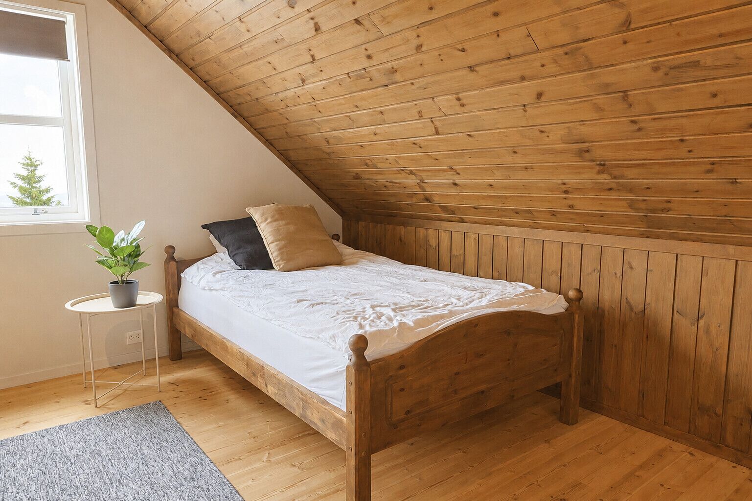 Een eenpersoonsbed met houten hoofdeinde in een kamer met schuine houten balken en een klein rond tafeltje met een plant.
