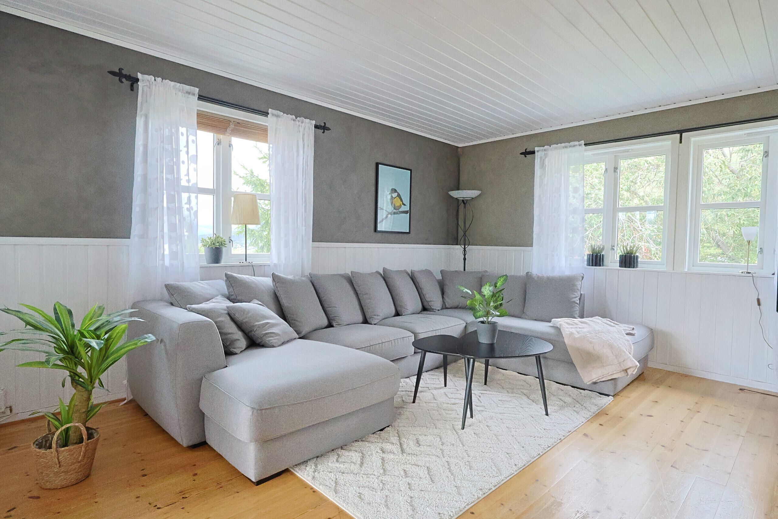 Ein modernes Wohnzimmer mit einem grauen Ecksofa, einem runden Couchtisch und einem weißen Teppich.