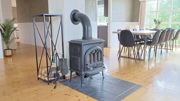 Une pièce avec un poêle à bois, une table à manger avec des chaises et une grande fenêtre.