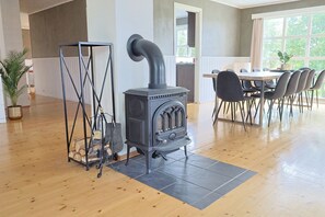 A room with a wood-burning stove, a dining table with chairs, and a large window.
