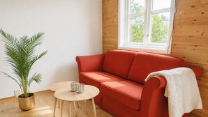 A red sofa, a small round table, and a potted plant in a room with wooden walls and a window. - Aurora House – A Family & Friends Retreat in Tromsø (Tromsø)