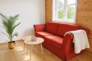 Ein rotes Sofa, ein kleiner runder Tisch und ein Blumentopf in einem Zimmer mit Holzwänden und einem Fenster.