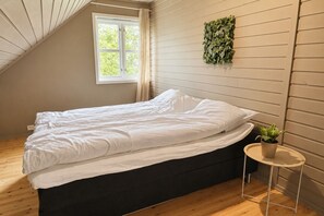 Un dormitorio con cama, ventana, planta en la pared y una pequeña mesa con planta.