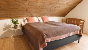 A bedroom with a sloped ceiling, a bed with a dark mattress and a brown blanket, two pillows, a small round table with a plant, and a wooden chair. - Aurora House – A Family & Friends Retreat in Tromsø (Tromsø)