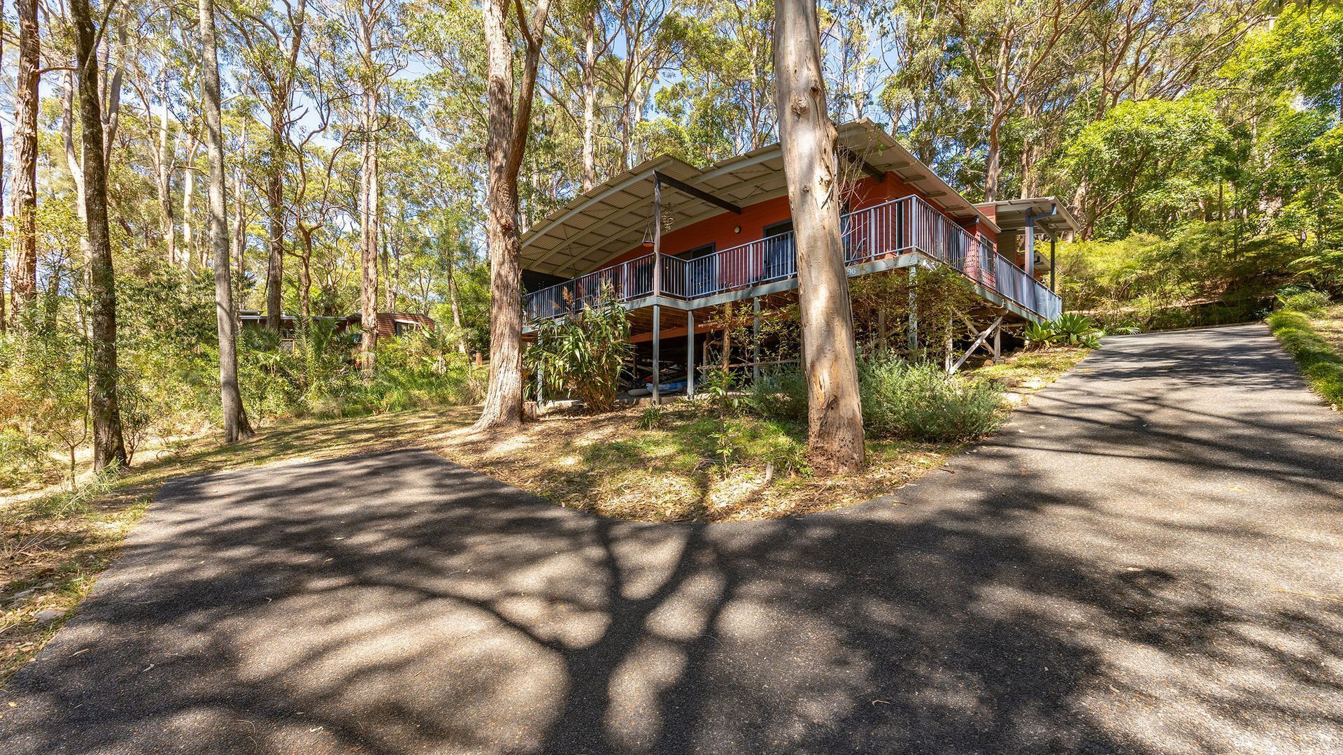Un bâtiment à deux étages doté d’un balcon, entouré d’arbres et bordé d’un chemin pavé.