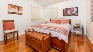Een slaapkamer met een houten bed, een nachtkastje, een stoel en kunstwerken aan de wanden.