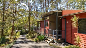 Eine rote Holzhütte mit Veranda, umgeben von Bäumen und einem Kiesweg.