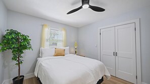 A bedroom with a bed, a ceiling fan, a window with blinds, a potted plant, and a door. - Cozy Cottage Mins to Siesta Key & Downtown, Hot Tub (Sarasota)