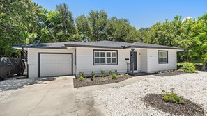 A single-story house with a garage, a covered porch, and a small front yard with gravel and plants. - Cozy Cottage Mins to Siesta Key & Downtown, Hot Tub (Sarasota)
