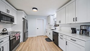 A modern kitchen with white cabinets, stainless steel appliances, and a black kettle on the stove. - Cozy Cottage Mins to Siesta Key & Downtown, Hot Tub (Sarasota)