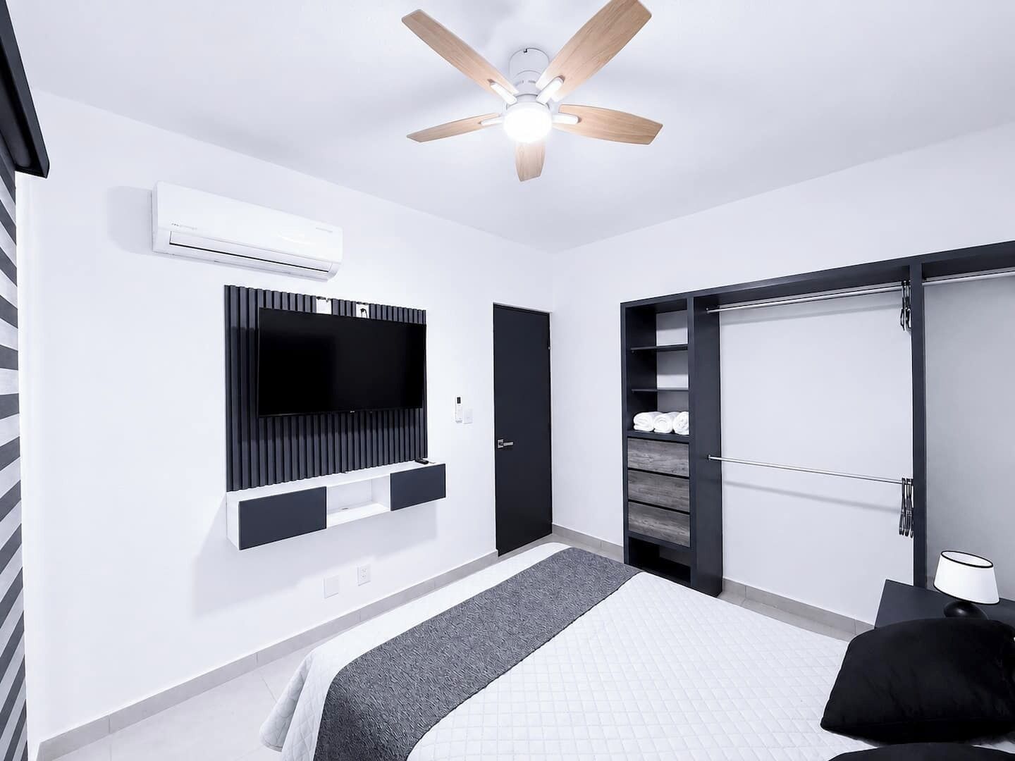 A modern bedroom with a bed, a television mounted on the wall, a ceiling fan, and a wardrobe with a sliding door.