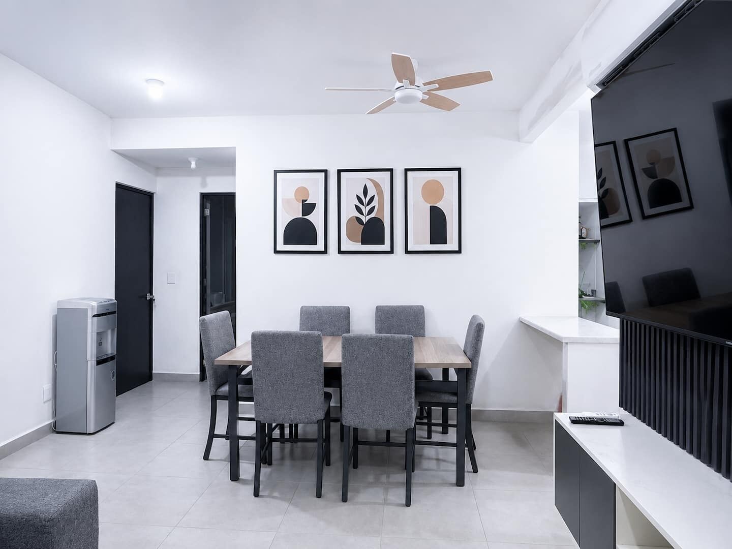 A modern dining area with a table and chairs, a ceiling fan, and framed artwork on the wall.