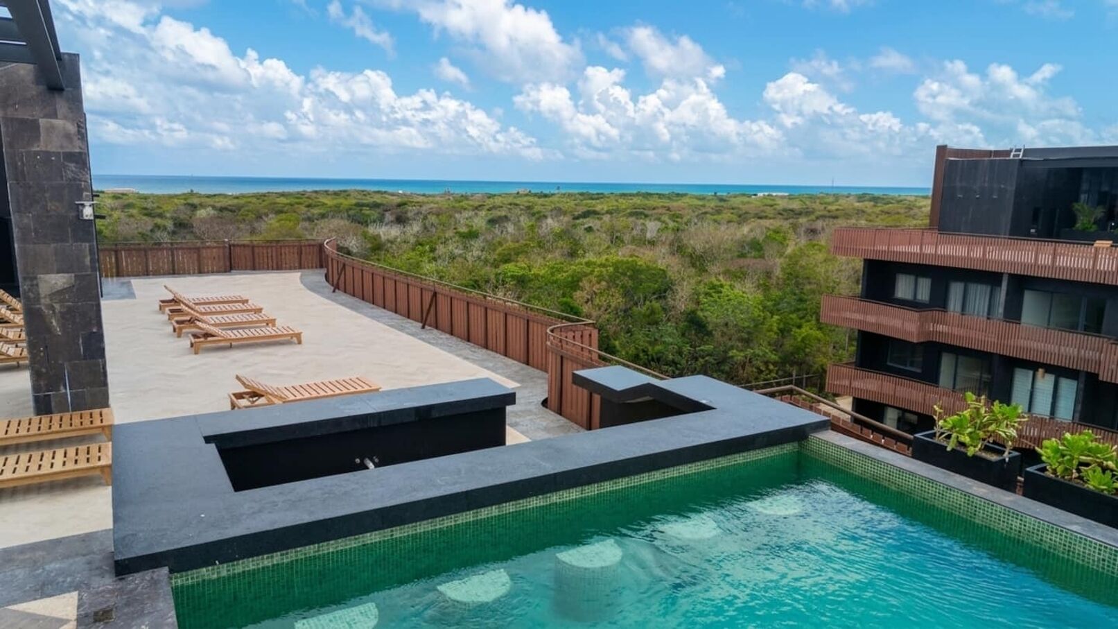 A rooftop pool with lounge chairs, a view of the ocean, and a building with a modern design.