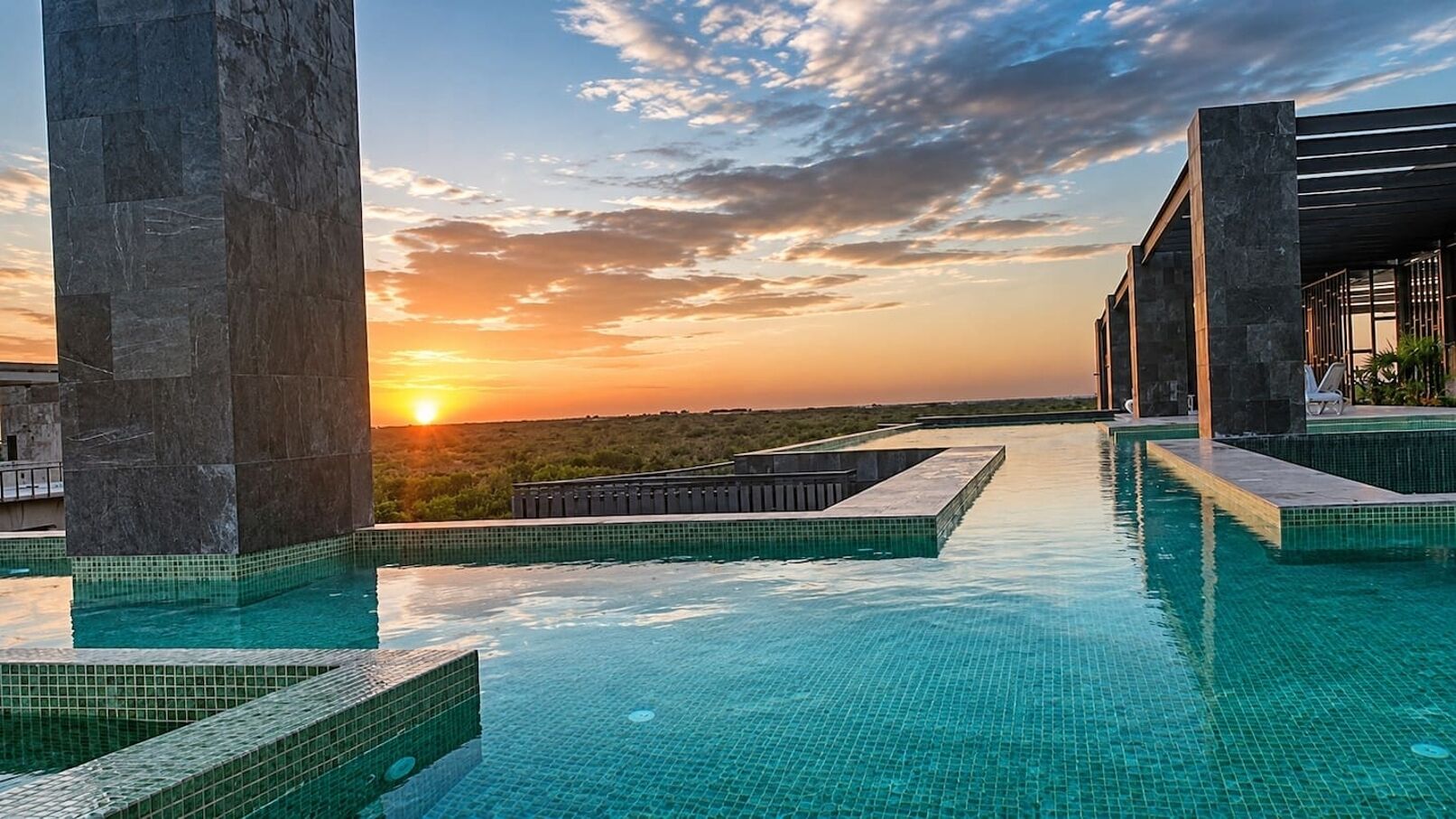 A rooftop infinity pool with a sunset view, surrounded by stone pillars and a modern architectural design.