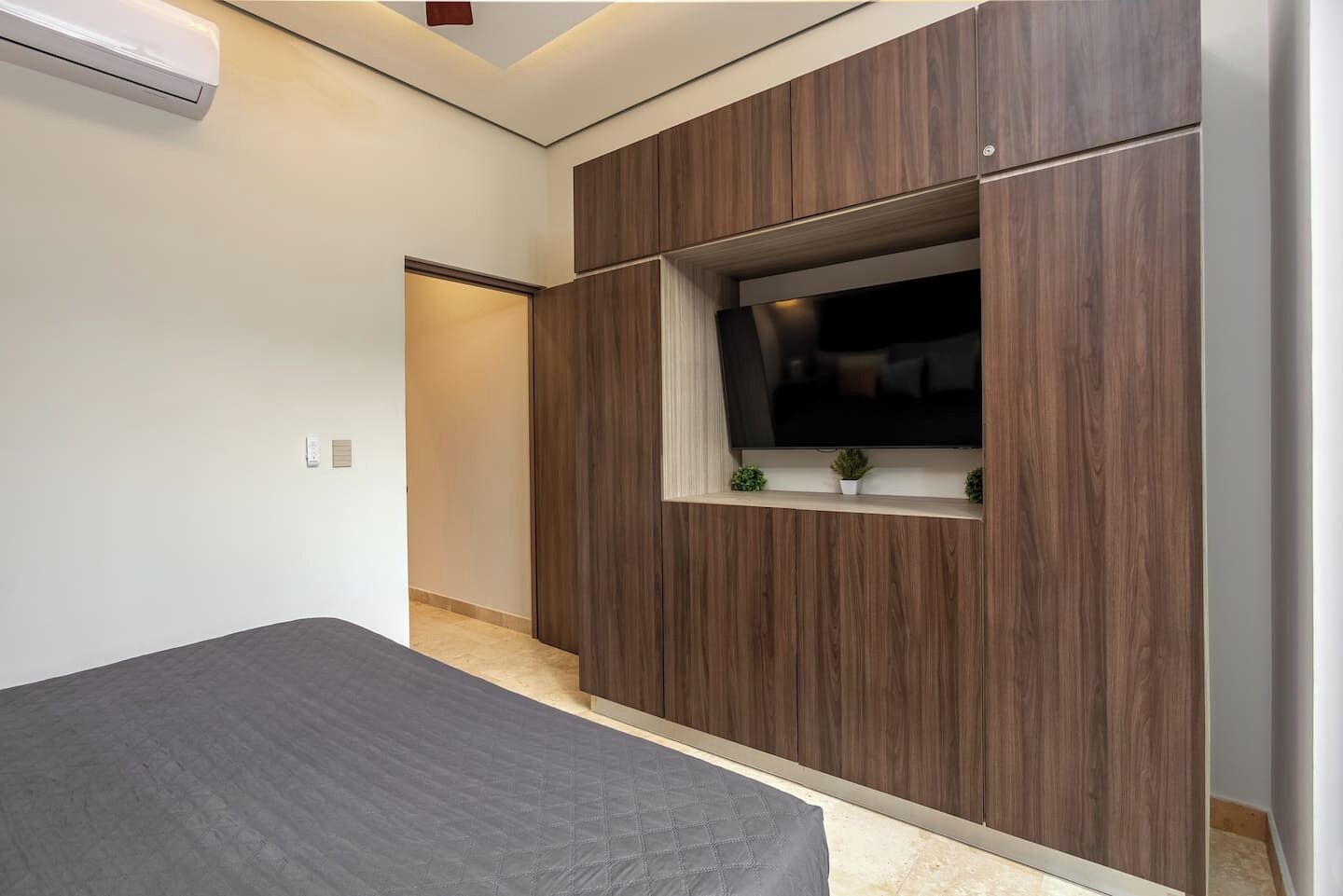 Une chambre à coucher avec un lit, un téléviseur fixé au mur en bois et une petite fenêtre.