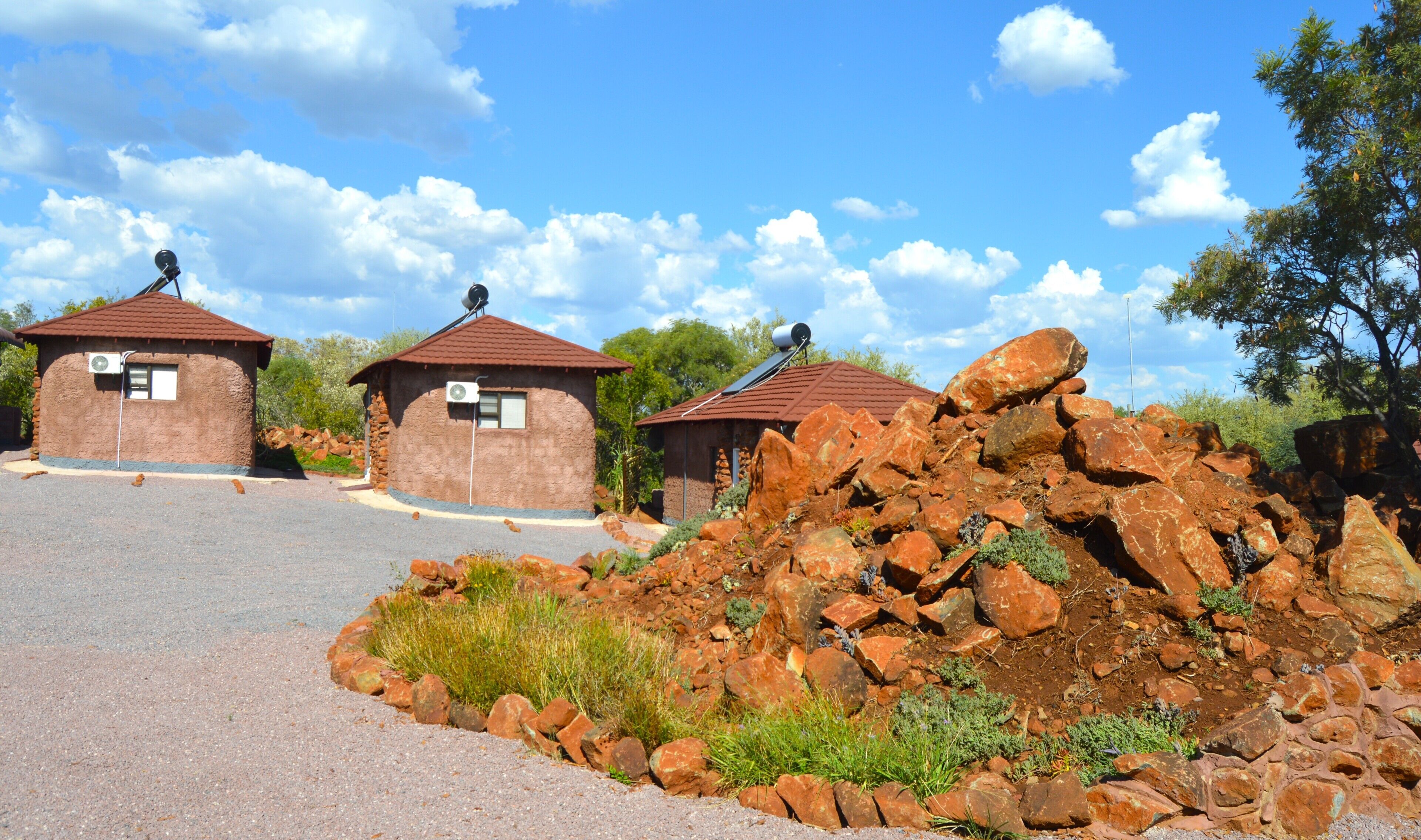 A building with a brown exterior and a red roof, surrounded by a gravel driveway and a pile of rocks.