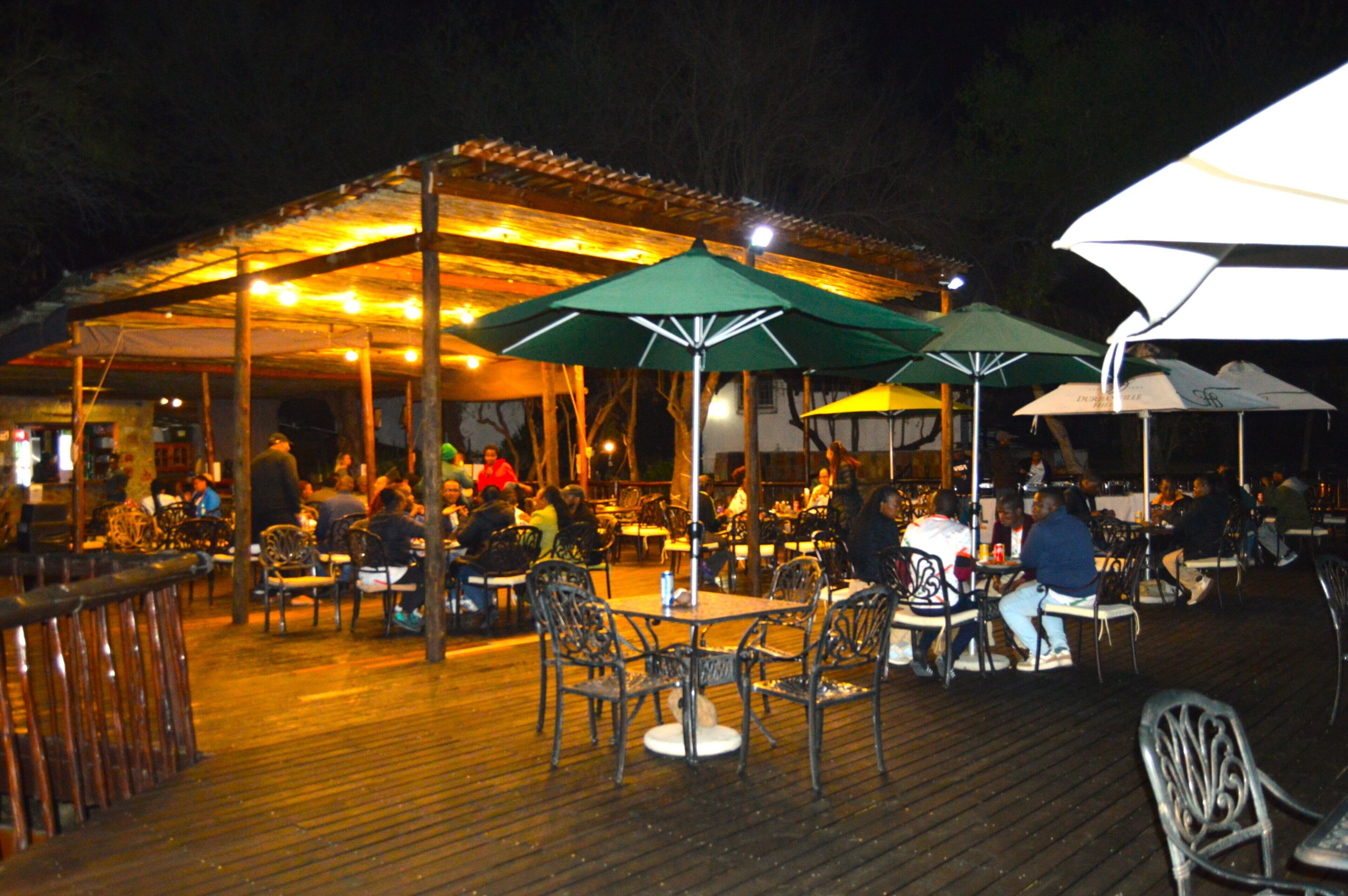 Un área de comedor al aire libre con mesas y sillas bajo sombrillas, rodeada por una terraza de madera.