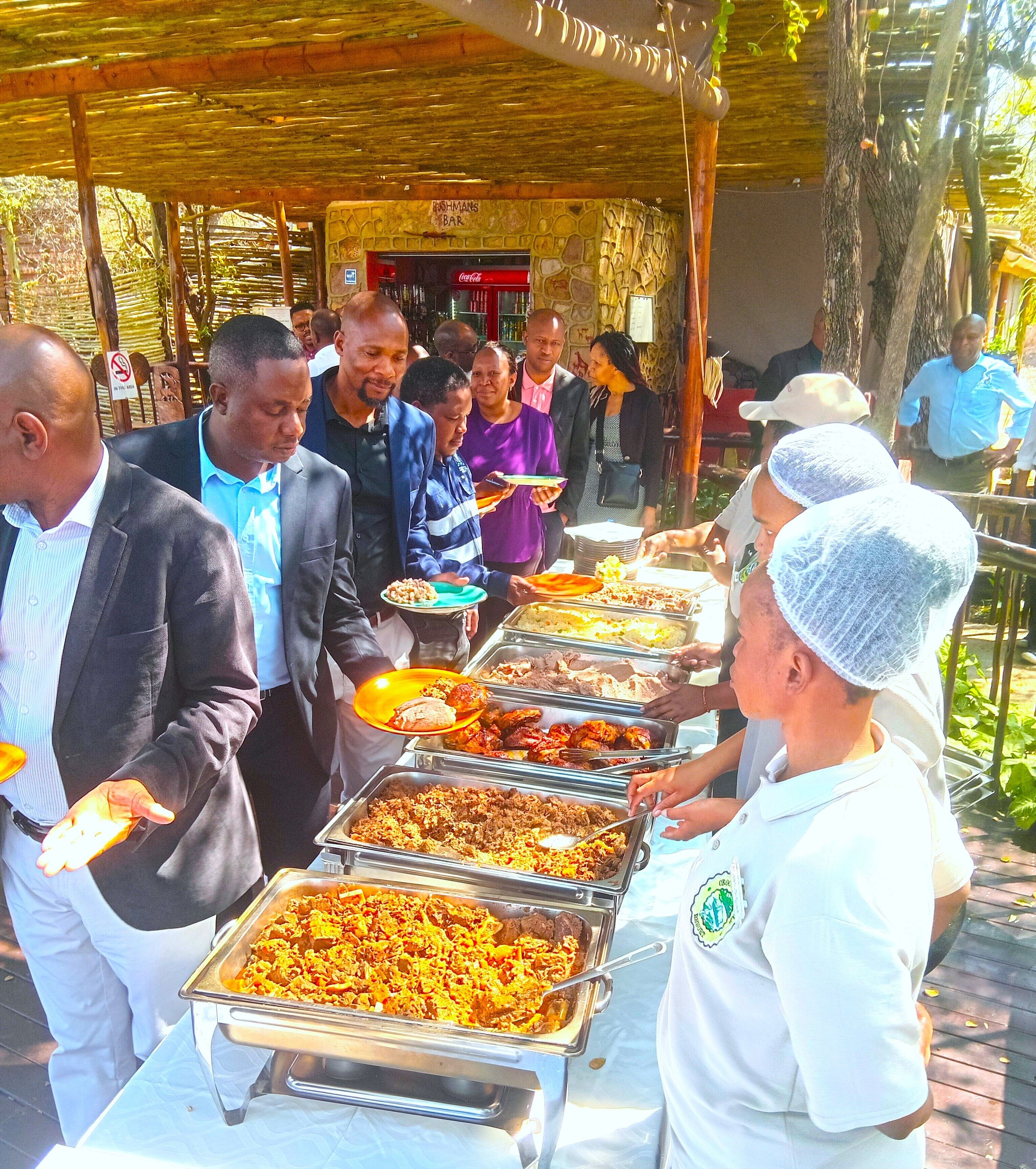 A buffet setup with various food items and people serving and serving food.