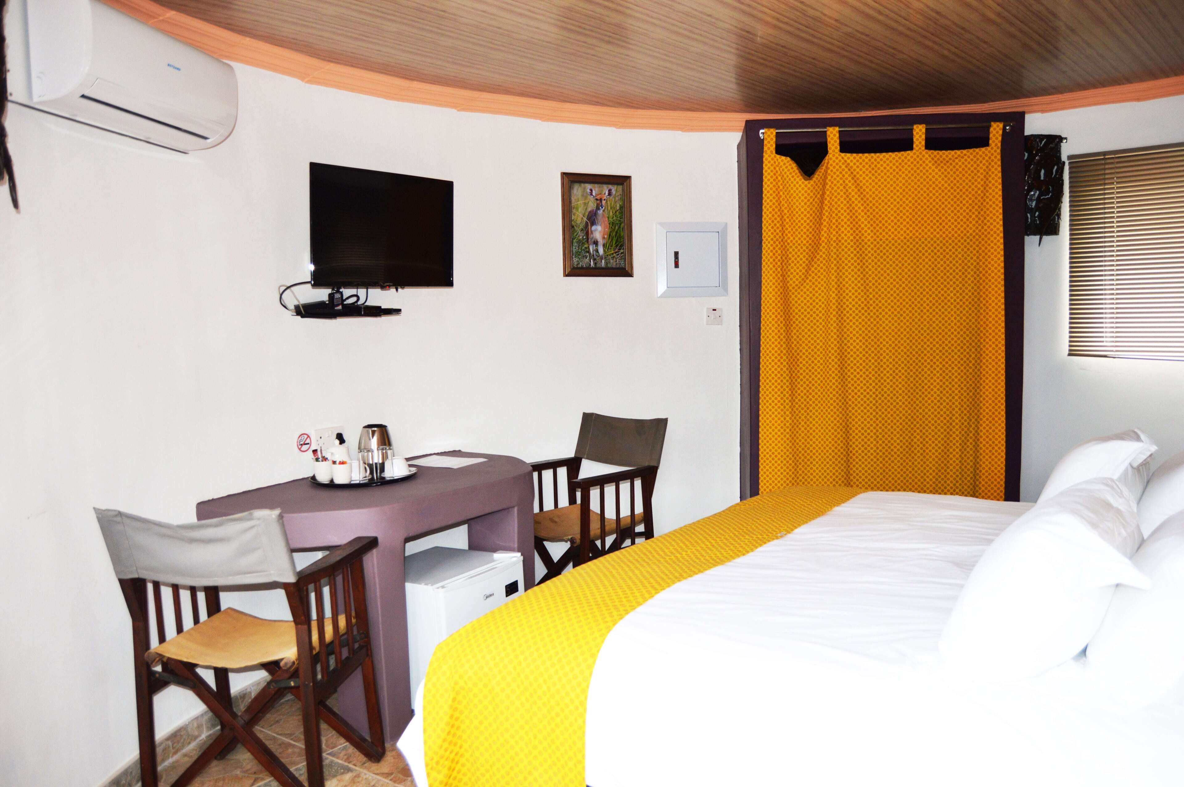 Una habitación de hotel con una cama, un escritorio con sillas, un televisor y una ventana con persianas.