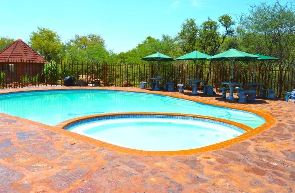 A swimming pool with a stone border, surrounded by tables and chairs, and a gazebo in the background.