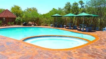 A swimming pool with a stone border, surrounded by tables and chairs, and a gazebo in the background.