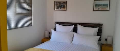 A single bed with white bedding and a yellow throw blanket, two bedside tables with lamps, and two framed pictures on the wall.
