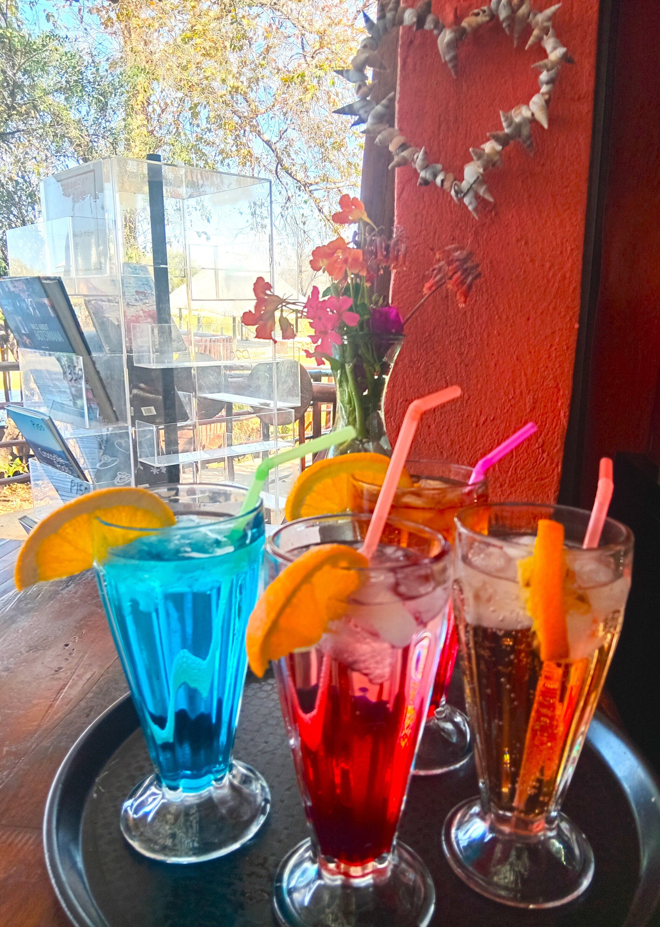 Three glasses of iced beverages with straws and orange slices on a tray.