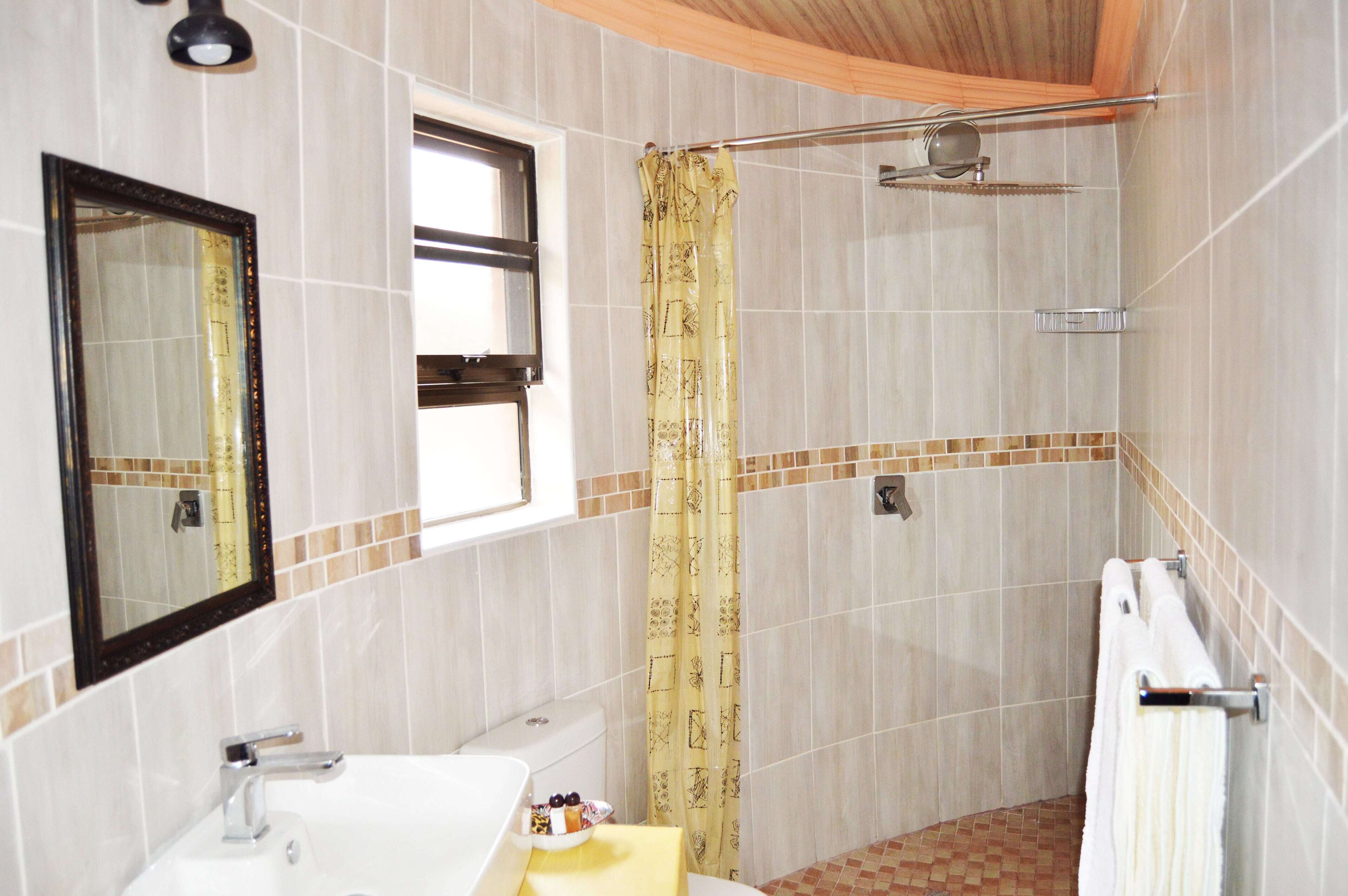 Une salle de bain comprenant des toilettes, un lavabo, un miroir, une douche et une fenêtre.