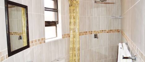 Une salle de bain comprenant des toilettes, un lavabo, un miroir, une douche et une fenêtre.