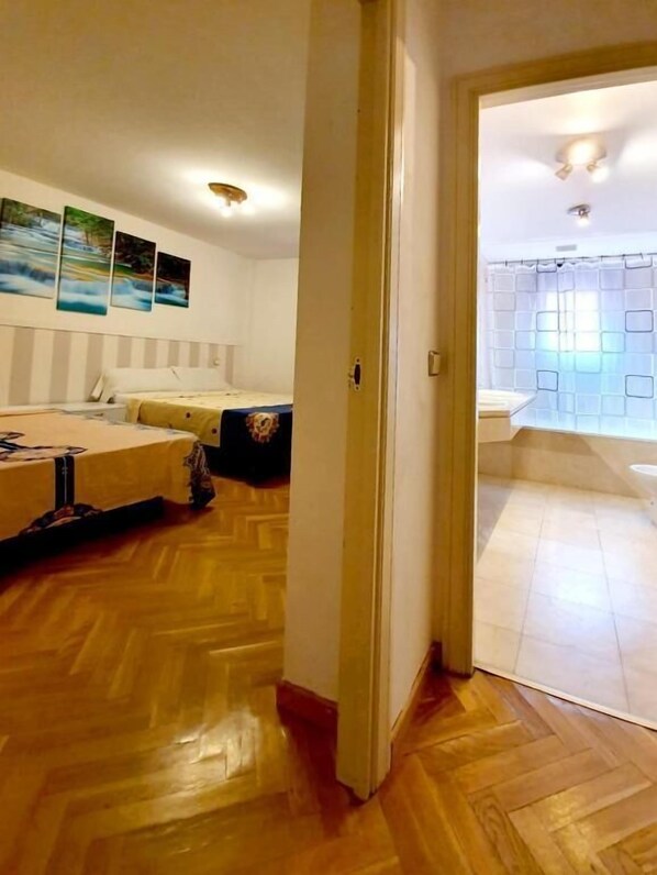 A room with a wooden floor, a bed with a headboard, a small table, and a wall with three framed pictures. - FUENCARRAL BARCELO ROOMS TPH (Madrid)
