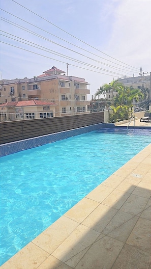 A swimming pool with a tiled edge, surrounded by a wooden deck and a tiled floor. - Relaxing condo walking distance to Beach and all your favorites things to do  . (Boca Chica)