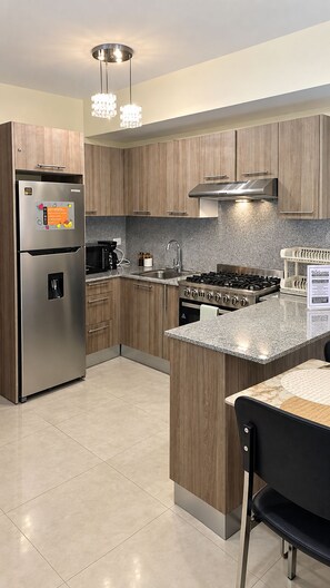 Eine moderne Küche mit Edelstahlgeräten, Holzschränken, einer Granitarbeitsplatte und einer integrierten Kücheninsel mit Sitzgelegenheit.