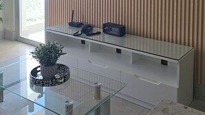 Ein modernes Wohnzimmer mit einem Flachbildfernseher an einer Wand aus Holzleisten, einem Glastisch und einer Topfpflanze.