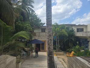 A courtyard with a palm tree, outdoor seating, and a building entrance. - Relaxing condo walking distance to Beach and all your favorites things to do  . (Boca Chica)