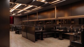 A modern restaurant interior with dark wood paneling, recessed ceiling lighting, and leather seating.