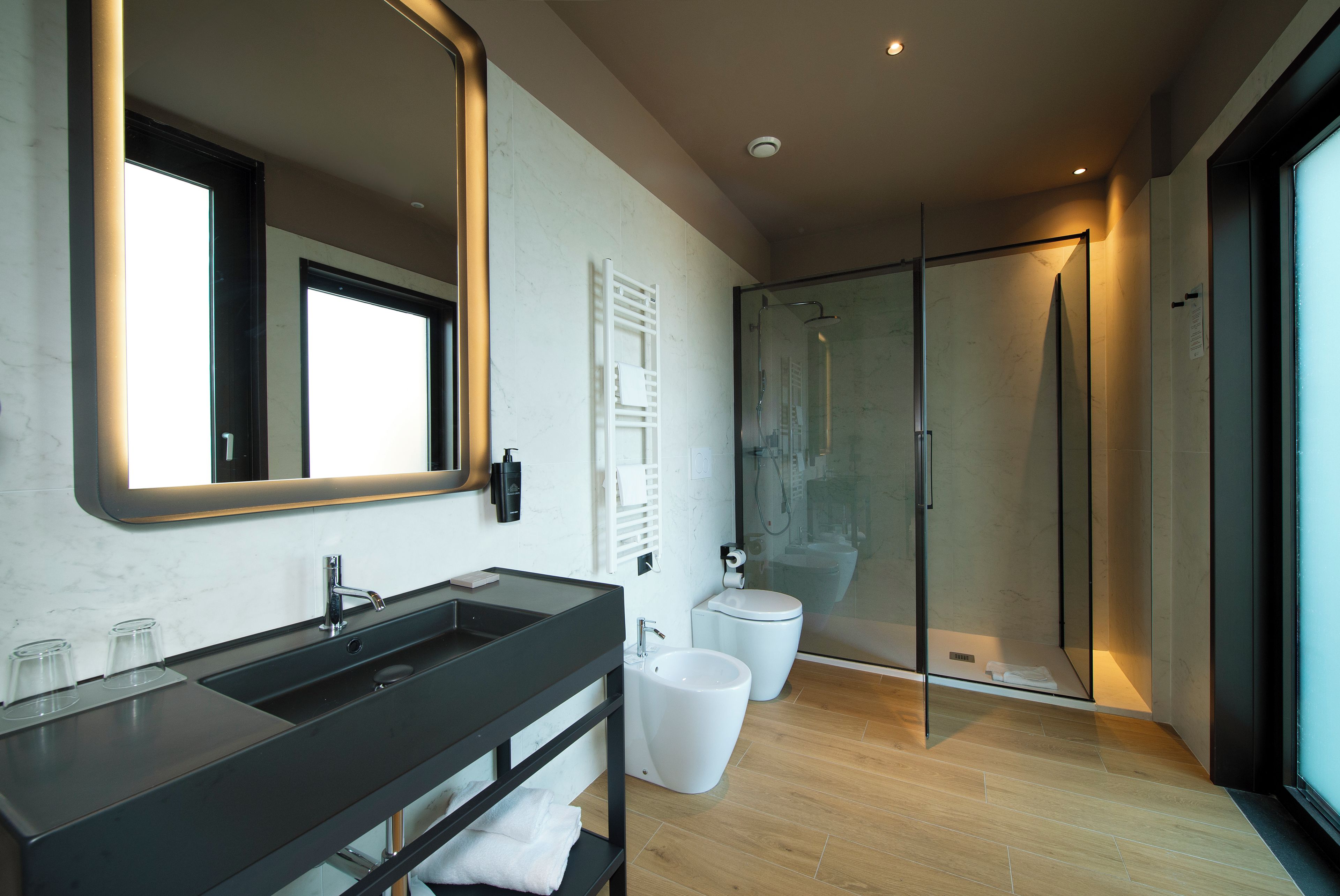 Un baño moderno con un espejo grande, lavamanos dobles, cabina de ducha de vidrio y suelo de madera.