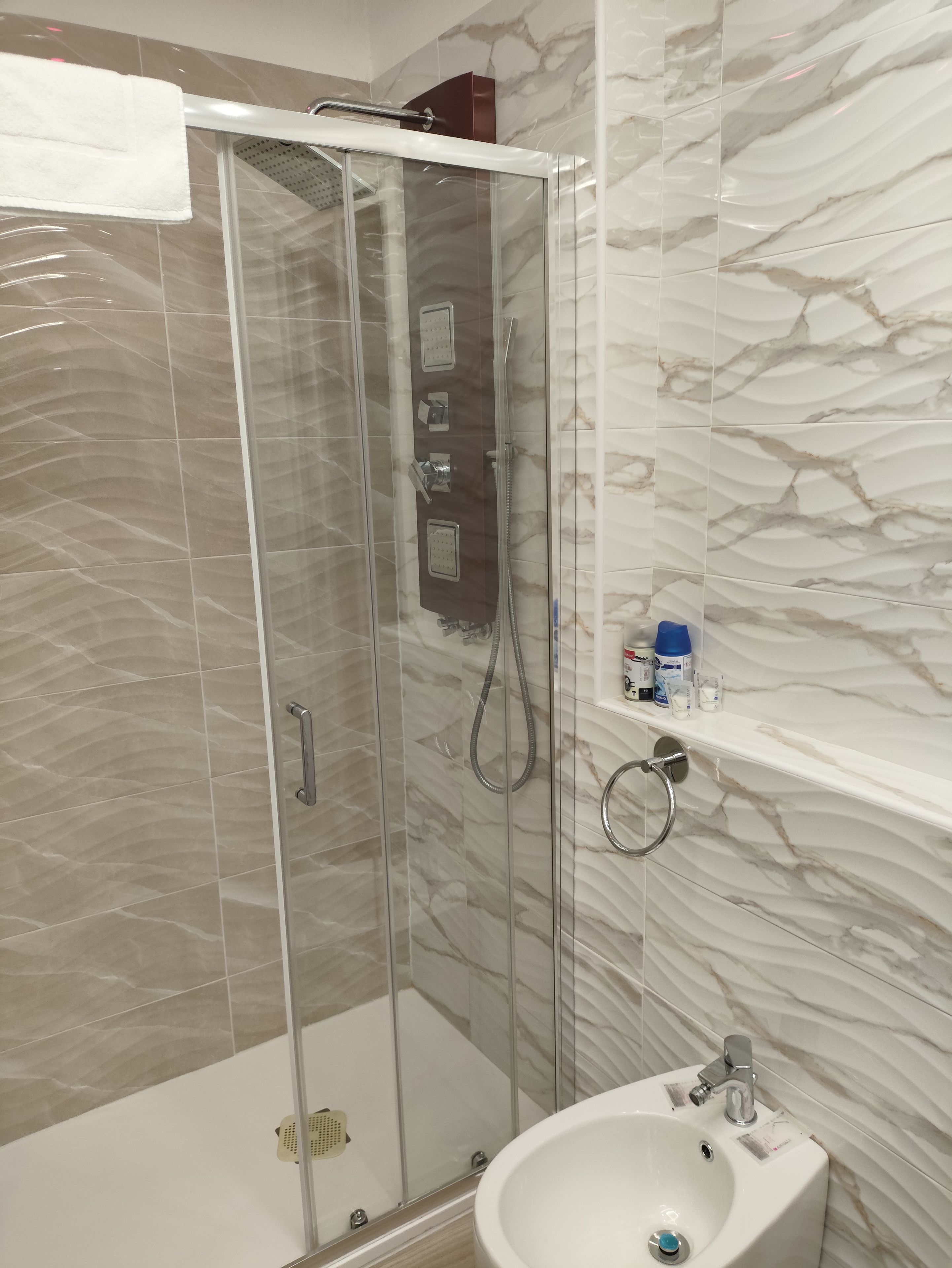 A modern bathroom with a glass-enclosed shower, a white sink, and marble-patterned walls.