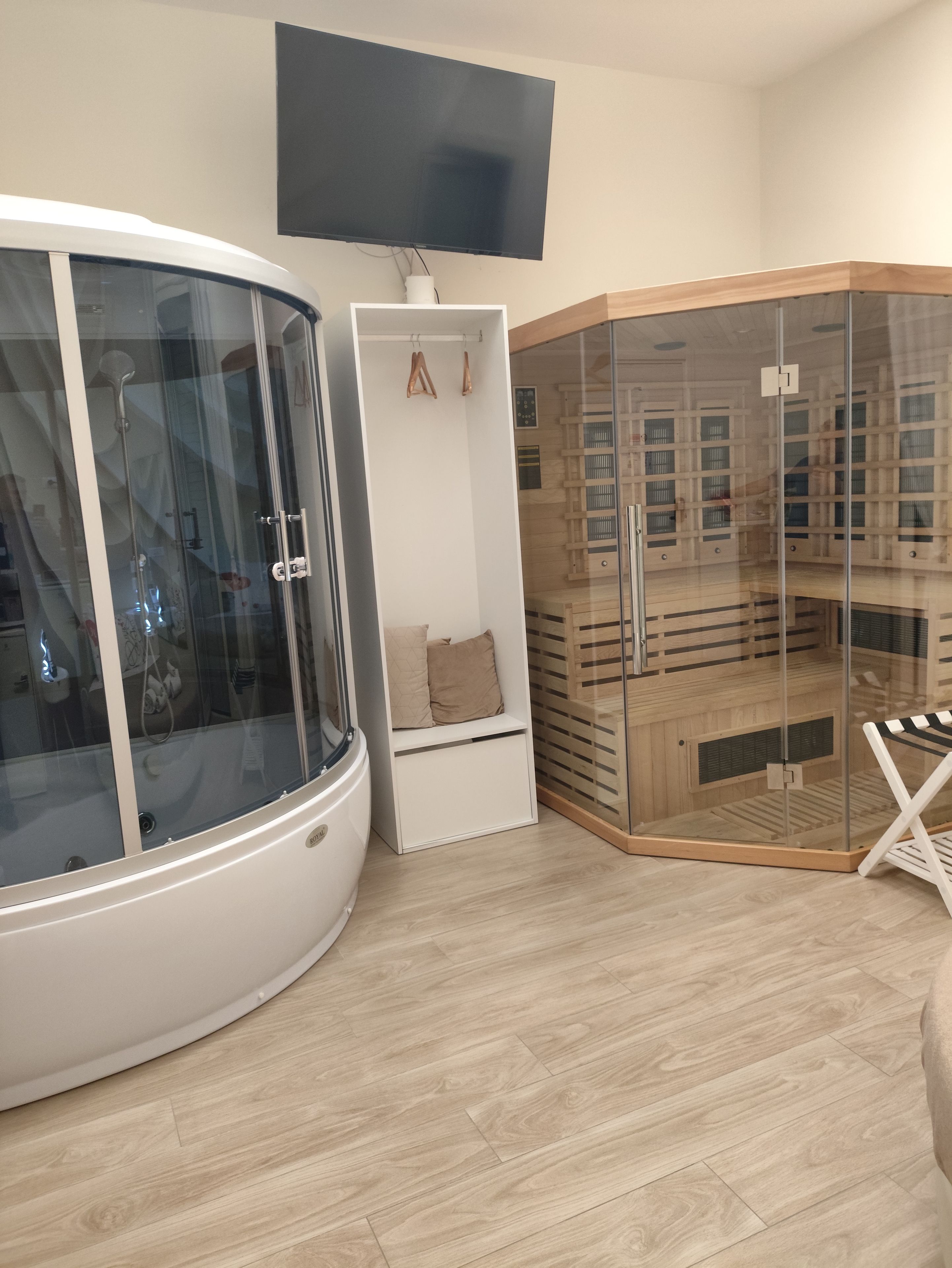 A modern room with a glass-enclosed sauna, a white cabinet with a bench, and a wooden sauna structure.