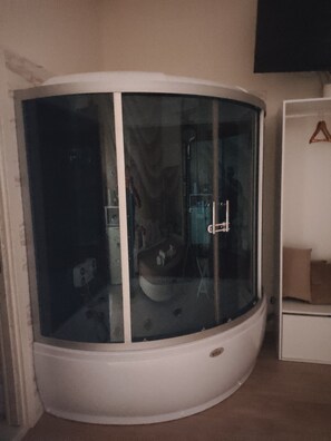 Una camera d'angolo con un armadietto bianco, una cabina doccia in vetro e un piccolo angolo relax.
