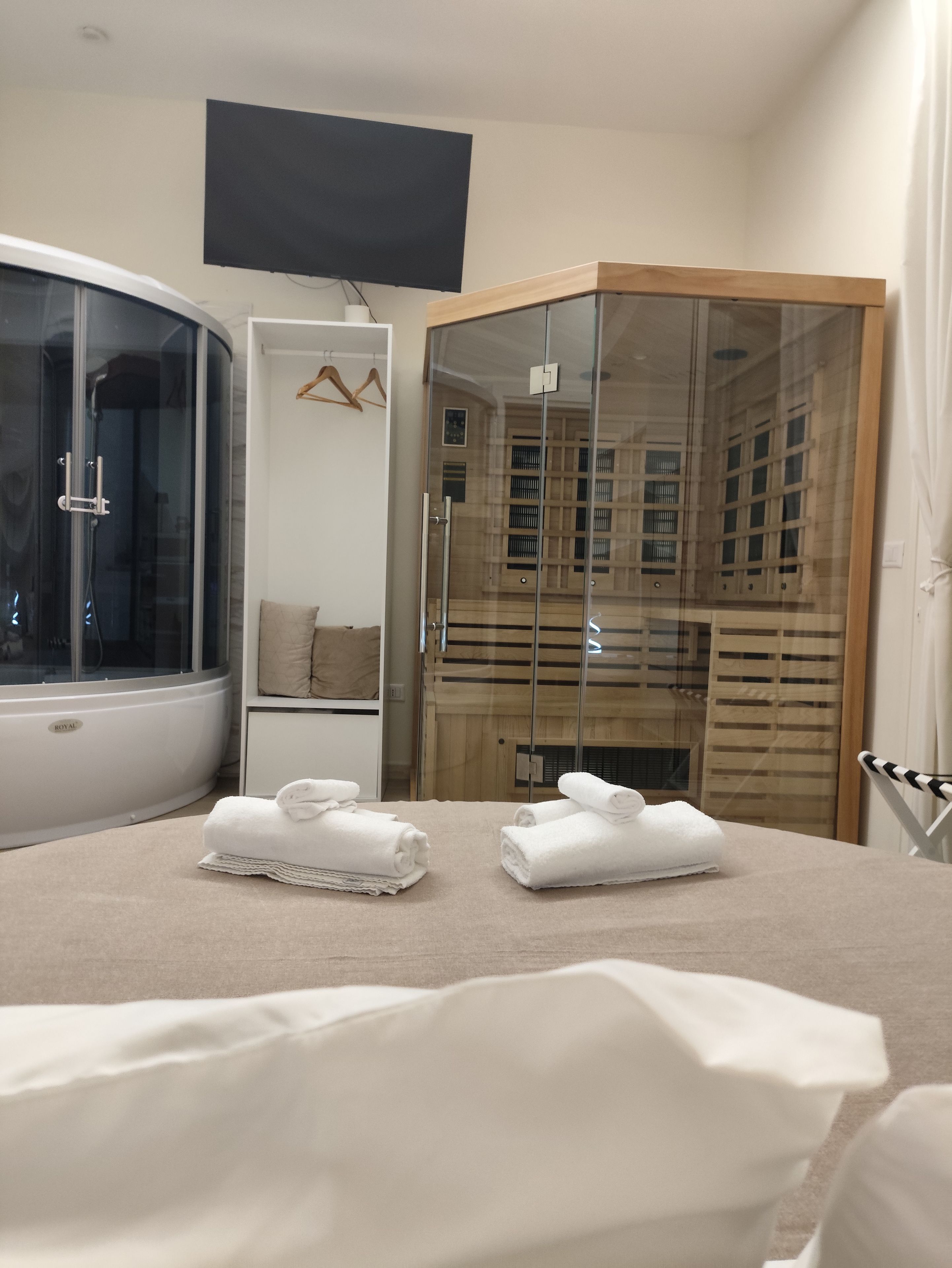 Une chambre d’hôtel avec un grand lit, une douche en verre, une armoire en bois et un téléviseur à écran plat fixé au mur.