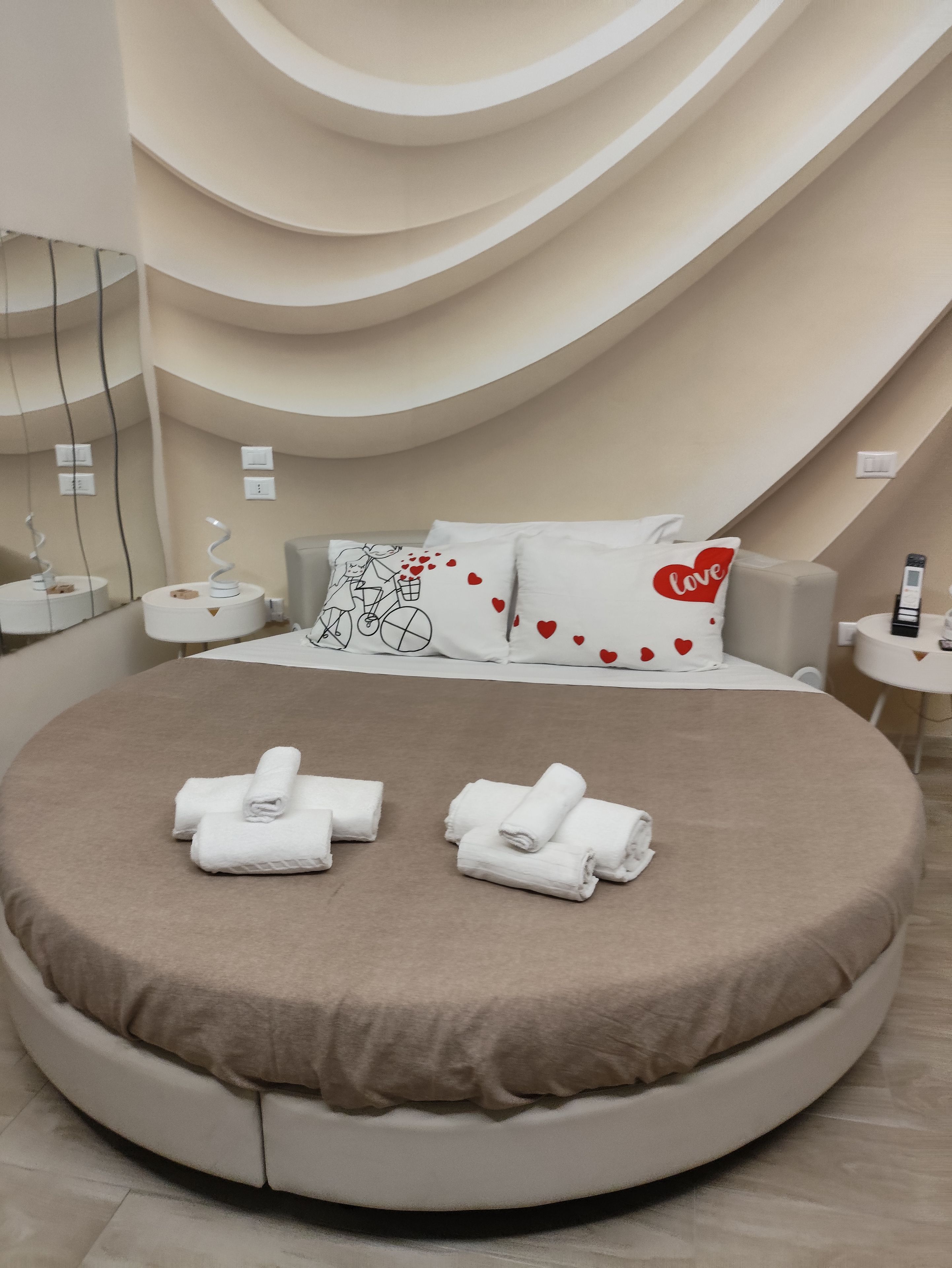 A modern bedroom with a circular bed, a mirror, and a wall with a heart pattern.