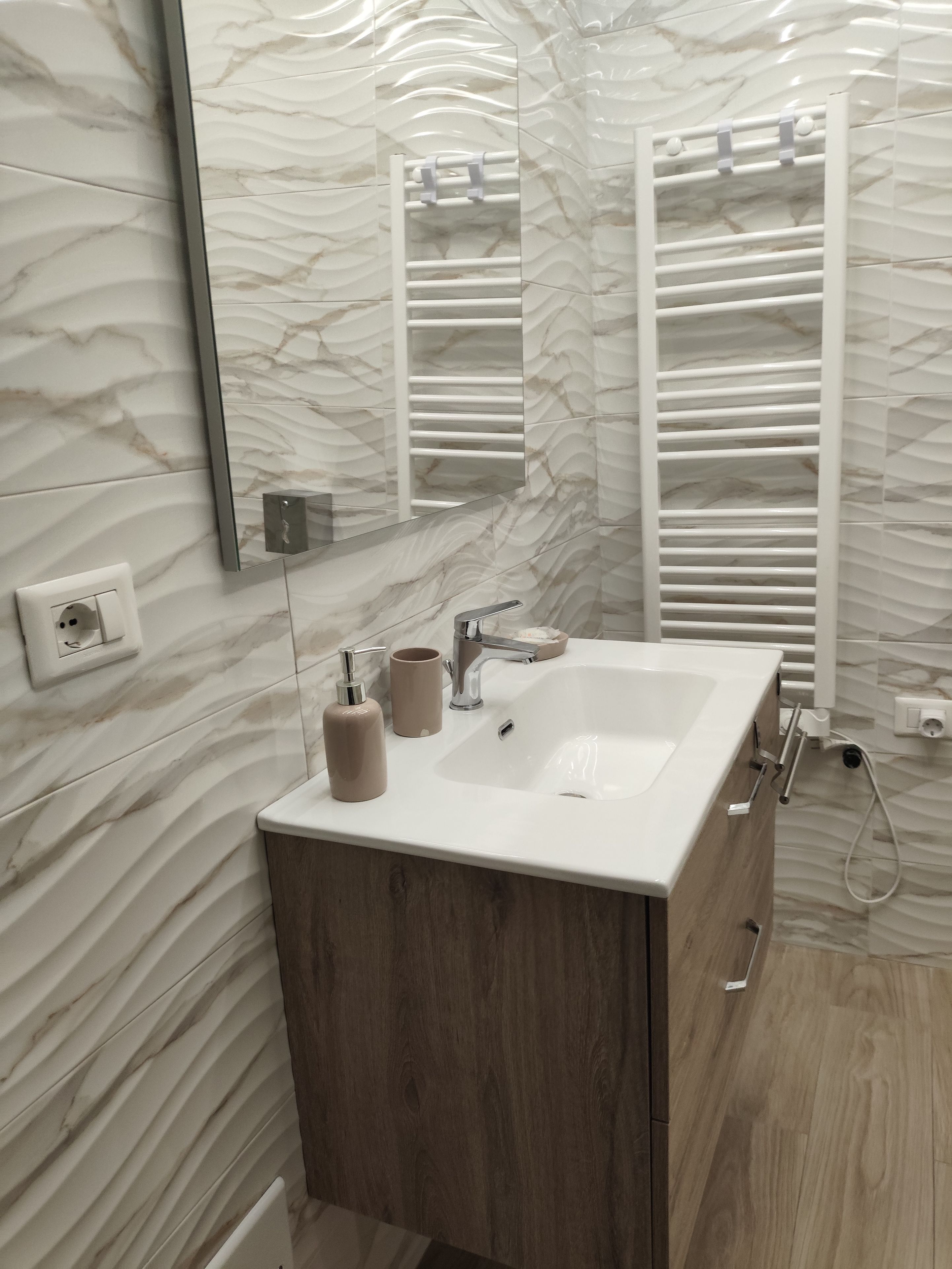 A bathroom with a marble wall, a white sink, a mirror, and a towel rack.