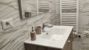A bathroom with a marble wall, a white sink, a mirror, and a towel rack.