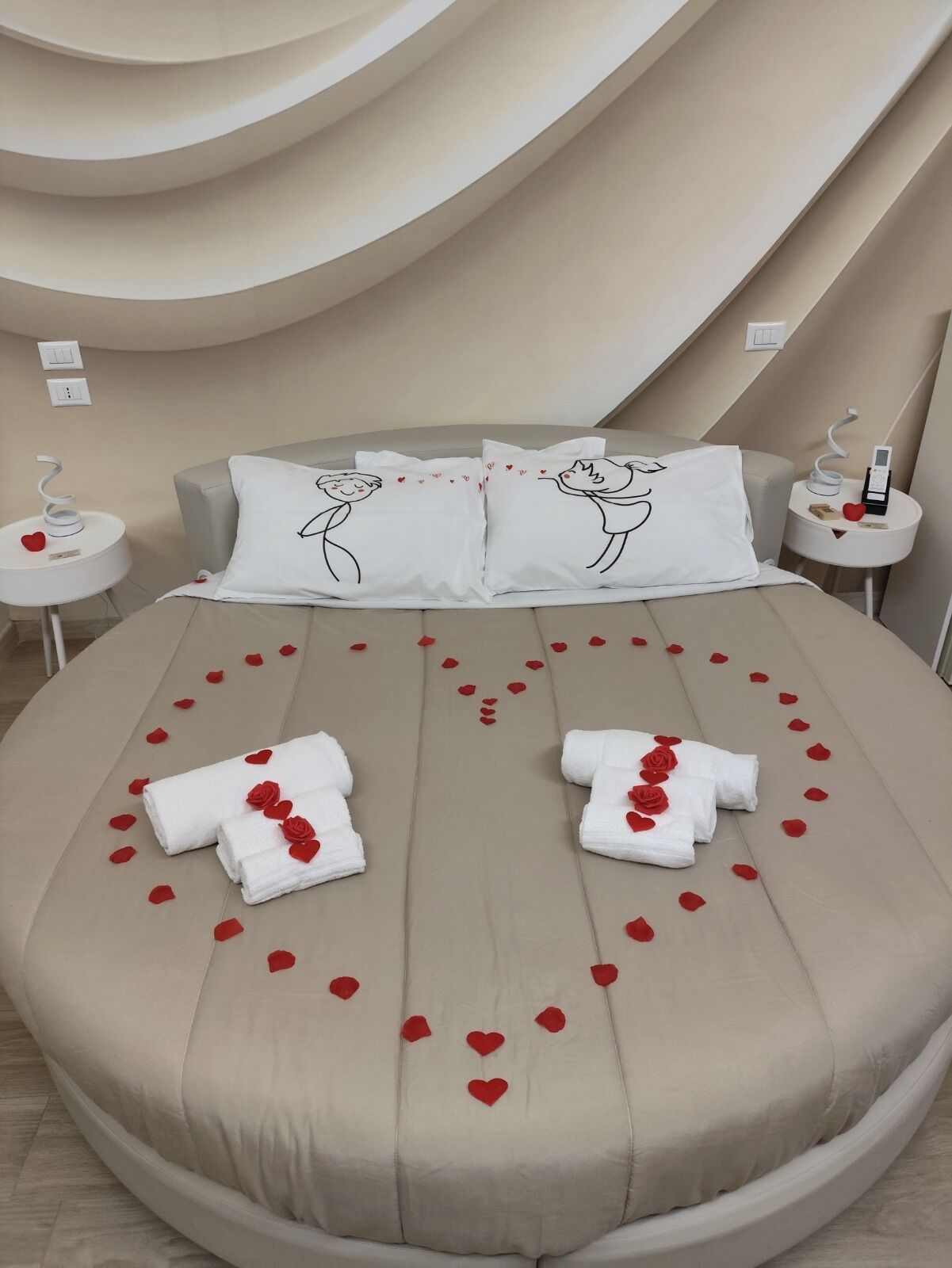Ein Bett mit Rosenblättern und Handtüchern, zwei Kissen mit einer Zeichnung eines Paares und ein modernes Zimmerdesign.