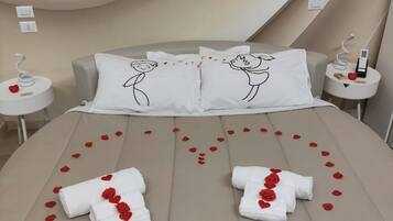 Ein Bett mit Rosenblättern und Handtüchern, zwei Kissen mit einer Zeichnung eines Paares und ein modernes Zimmerdesign.