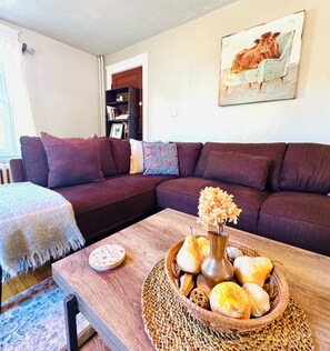 A living room with a sectional sofa, a coffee table with a decorative centerpiece, and a bookshelf in the background. - Ancestral Charming Home - Central Downtown Charlottetown (Charlottetown)
