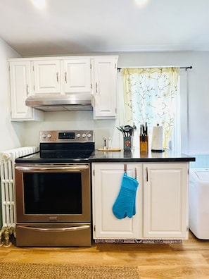 A kitchen with white cabinets, a stainless steel oven, a black countertop, and a blue oven mitt hanging on the door. - Ancestral Charming Home - Central Downtown Charlottetown (Charlottetown)