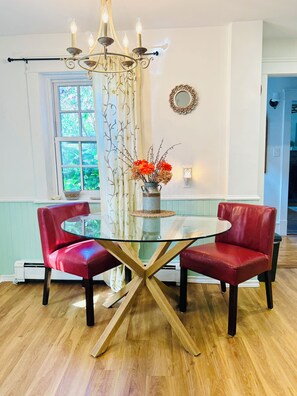 A dining area with a glass table, two red chairs, a chandelier, and a vase with flowers. - Ancestral Charming Home - Central Downtown Charlottetown (Charlottetown)
