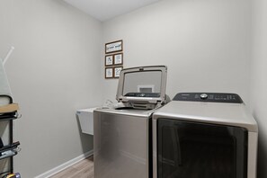 A laundry room with a front-loading washer and dryer, a wall-mounted drying rack, and a sign above the dryer.